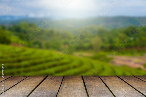 Wooden floor with beautiful sunset blur image of tea plantation background.