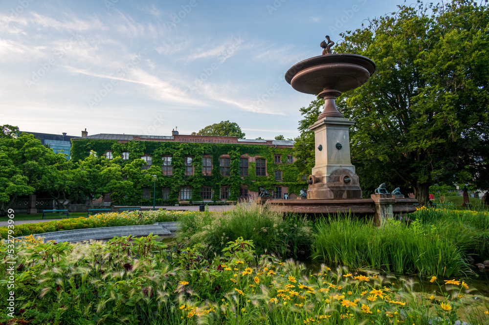Obraz premium Green foliage around the fountain at the park in front of the old university building during summer in Lund Sweden