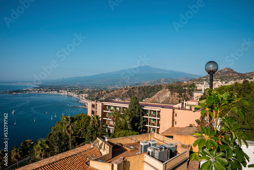 Beautiful view of famous Etna Volcano and luxurious Elios hotel. Popular tourist attraction by seascape with blue sky in background. Picturesque scenery of city during summer. photo