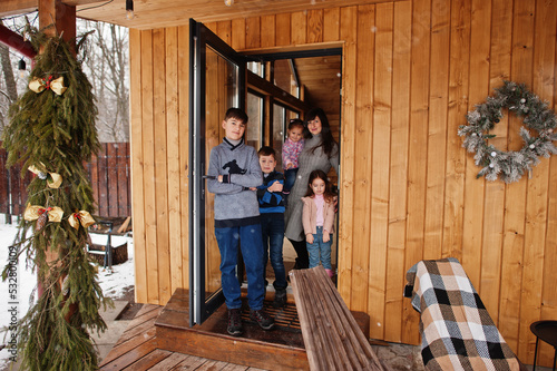 Mother and kids in modern wooden house stand near door entrance.