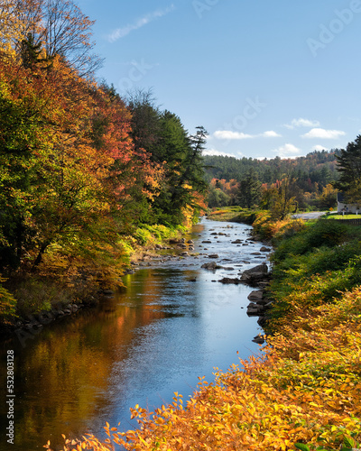 A beautiful river next to the highway in rural Vermont surrounded by a forest in beautiful autumn color. 