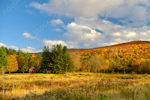A beautiful rural scene in Vermont in the autumn. There is a red house at a homestead with mountains in the background.  photo