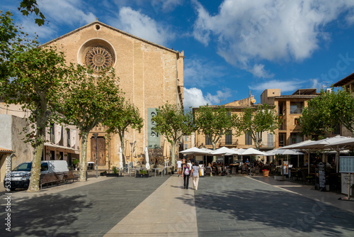 Tourists walking between restaurants, next to the Mare de Déu dels Angels church, in the Plaza Mayor of Pollença (Mallorca, Spain) on a summer morning photo