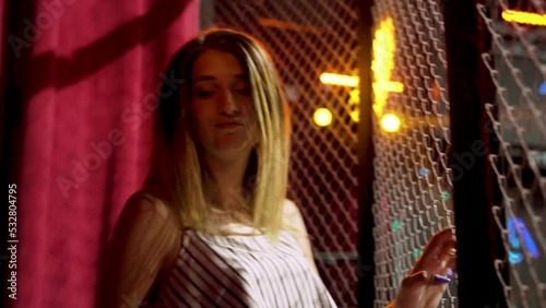 Sexy young caucasian blond girl dances in night club cage with metal bars