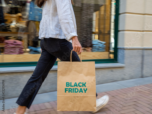 Picture in movement of a girl walking hurriedly with a shopping bag in front of a shop window. Shopping day, bargains, black friday.