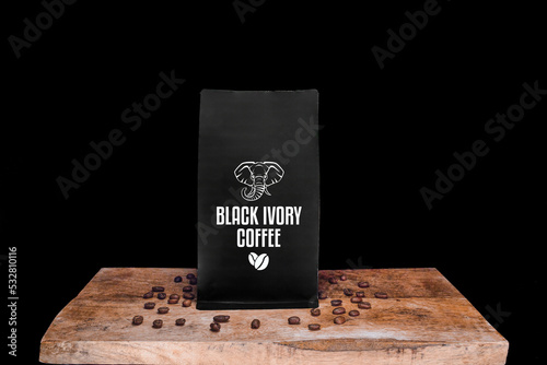 Black Ivory coffee beans and black package on wooden board with black isolated background