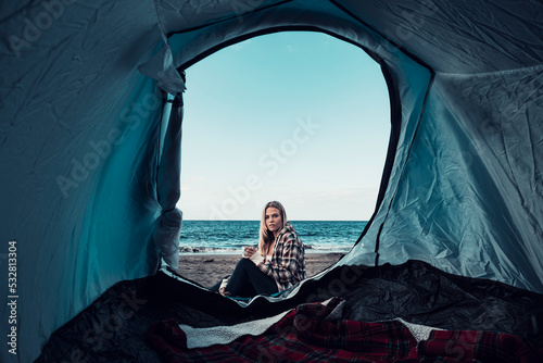 One traveler viewed from inside a tent in free beach camping lifestyle. Concept of solo woman in travel. Freedom and alternative holiday summer vacation. One young girl outdoor enjoying trip
