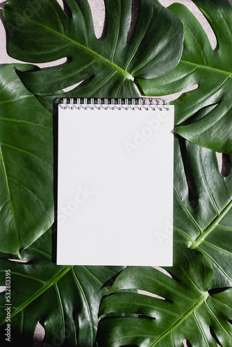 Blank notepad page on monstera leaves tropical background. Vertical mockup