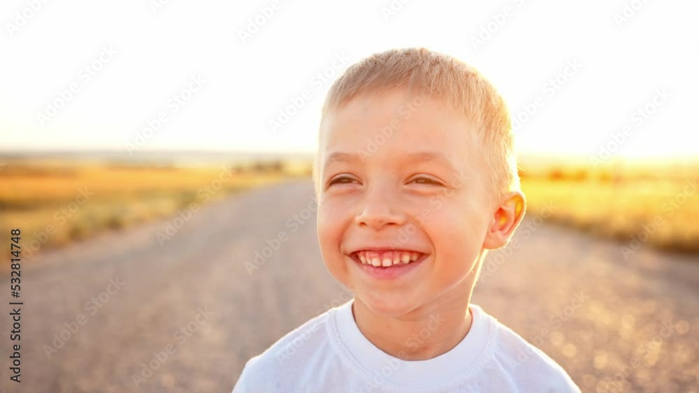 Close up portrait and face of caucasian baby boy. Child stands on asphalt road next to wheat fields. Kid happy smiling and toothy laughs on walk in sun rays. Nature landscape. Leisure activity. Rest. Close up portrait and face of caucasian baby boy. Child stands on asphalt road next to wheat fields. Kid happy smiling and toothy laughs on walk in sun rays. Nature landscape. Leisure activity. Rest.