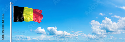 Belgium flag waving on a blue sky in beautiful clouds - Horizontal banner