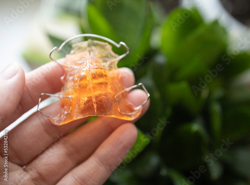 an apparatus for correcting the bite in children, in the hand of a girl, against the background of a houseplant, in daylight. Hygiene, dental treatment, bite correction, new technologies.