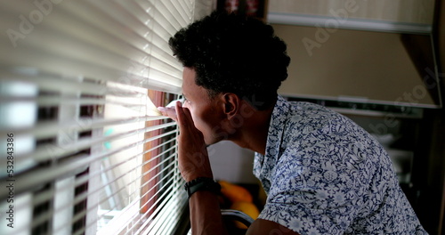 Fotografie African man looking through window blinds