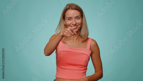 I choose you. Blonde pretty woman pointing to camera and looking with playful happy expression, making choice, showing direction. Young adult slim thin slender girl isolated on blue studio background