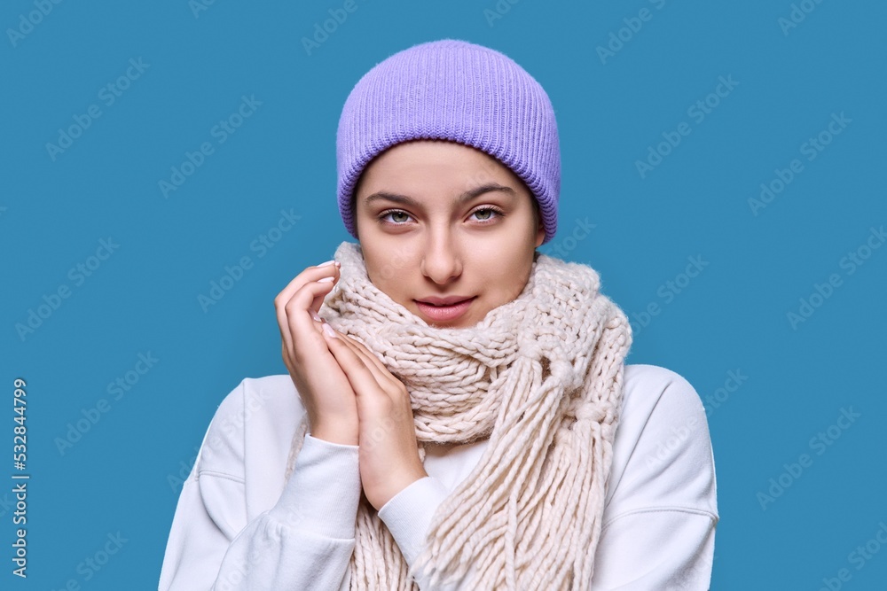 Winter portrait of young female in sweater hat scarf, on blue studio background Winter portrait of young female in sweater hat scarf, on blue studio background
