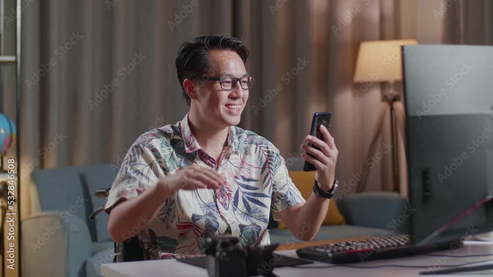 Asian Man In Wheelchair Waving Hand And Having A Video Call On Smartphone While Editing The Video By A Desktop Next To The Camera At Home
Asian Man In Wheelchair Waving Hand And Having A Video Call On Smartphone While Editing The Video By A Desktop Next To The Camera At Home