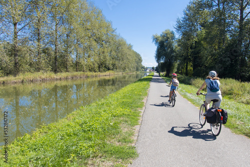 maman et sa fille en train de faire du vélo sur une piste cyclable le long d'un canal en été