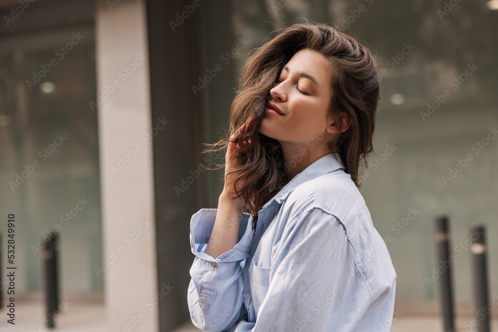 Tender young caucasian brunette woman closing her eyes posing outdoors. Beauty wears blue shirt. Relaxation concept Tender young caucasian brunette woman closing her eyes posing outdoors. Beauty wears blue shirt. Relaxation concept