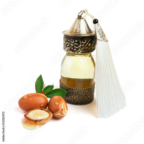 Argan oil in a oriental glass and metal bottle and argan nuts with green leaves isolated on white background. photo