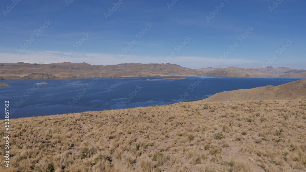 Un grand désert de verdure sèche péruvien, avec un grand lac bleu tranquille et plat, des montages et du soleil, de la chaleur torride