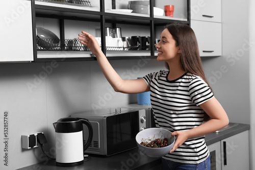Photos Happy young woman with bowl of cherries in hostel kitchen