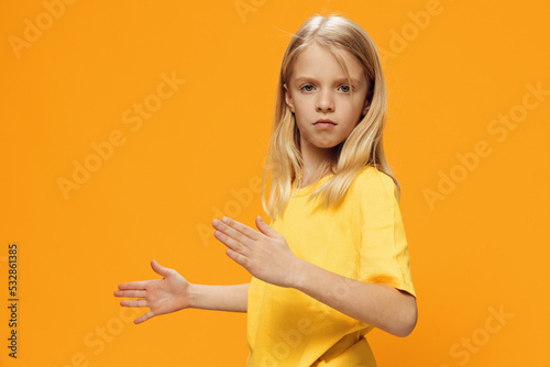 a cute, beautiful school-age girl in yellow clothes stands on a bright background in a robot pose