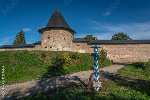 View of the Izborskaya Tower of the Holy Dormition Pskov-Pechersk Monastery and a memorial sign to the First International Postal Route on a sunny summer day, Pechory, Pskov region, Russia photo