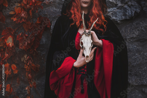 Red-haired beautiful young woman witch conjures and holds a goat skull in her hands. witches coven for halloween. Unrecognizable  photo