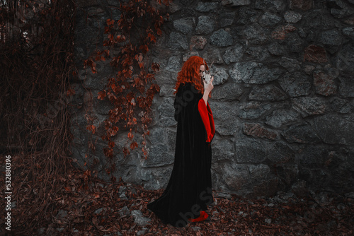 Red-haired beautiful young woman witch conjures and holds a goat skull in her hands. witches coven for halloween photo