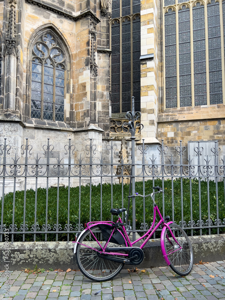 Purple bicycle lay against a wrought iron fence around an old stone church with stained glass windows
