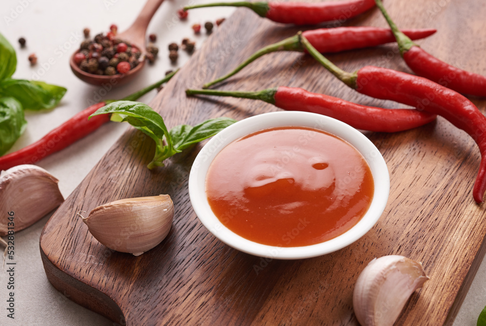 red hot chilli sauce. tomato ketchup, chilli sauce, puree with chili pepper, tomatoes and garlic. on wooden cutting board on stone background. top view. red hot chilli sauce. tomato ketchup, chilli sauce, puree with chili pepper, tomatoes and garlic. on wooden cutting board on stone background. top view.
