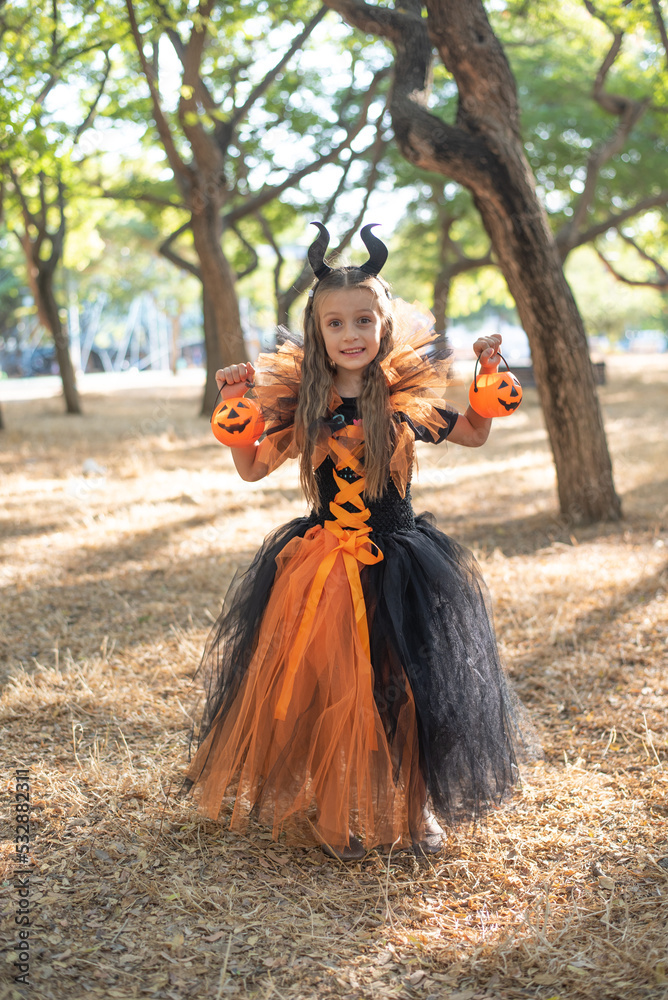 Happy child girl in costume of evil trick or treat with pumpkin baskets in hands. on background of scary autumn forest. outdoors in halloween Happy child girl in costume of evil trick or treat with pumpkin baskets in hands. on background of scary autumn forest. outdoors in halloween