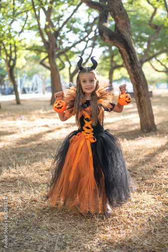 Happy child girl in costume of evil trick or treat  with pumpkin baskets in hands. on background of scary autumn forest. outdoors in halloween