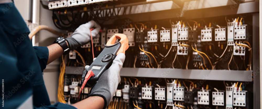 Electricity or electrical maintenance service, Engineer hand holding voltmeter checking electric current voltage at circuit breaker terminal and cable wiring main power load center distribution board.