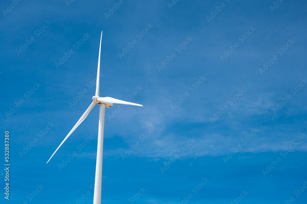 Electricity generating white large wind turbine standing against blue sky background in a windy zone area in southeast Asia.