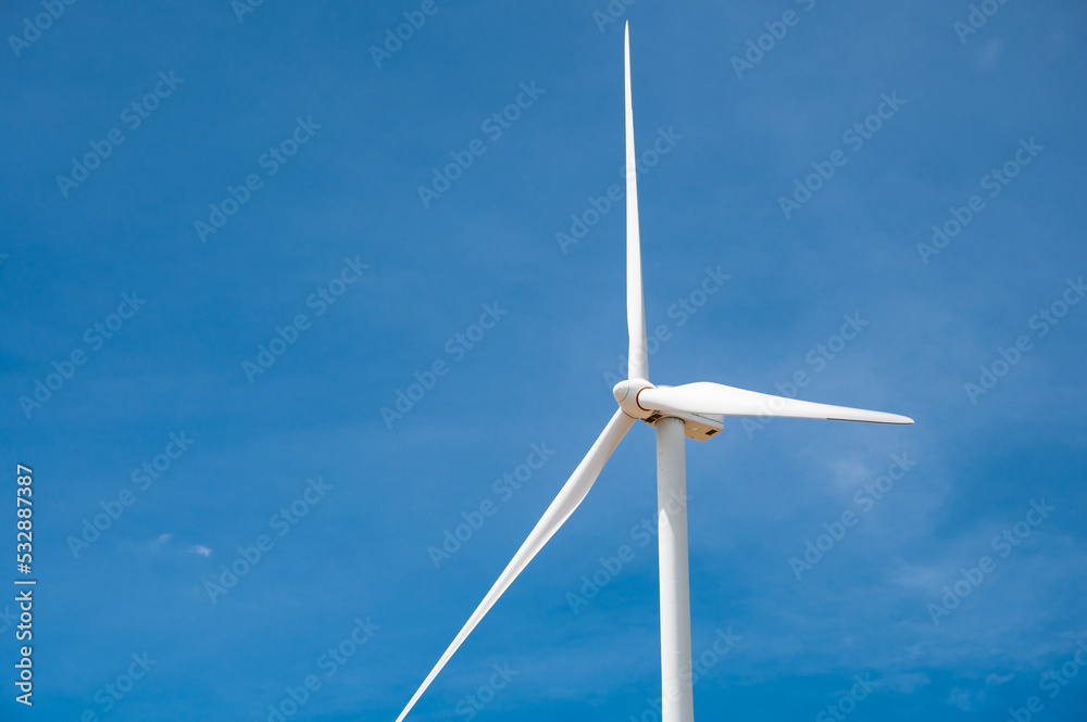 Electricity generating white large wind turbine standing against blue sky background in a windy zone area in southeast Asia. Electricity generating white large wind turbine standing against blue sky background in a windy zone area in southeast Asia.
