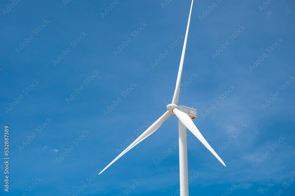 Electricity generating white large wind turbine standing against blue sky background in a windy zone area in southeast Asia. Electricity generating white large wind turbine standing against blue sky background in a windy zone area in southeast Asia.