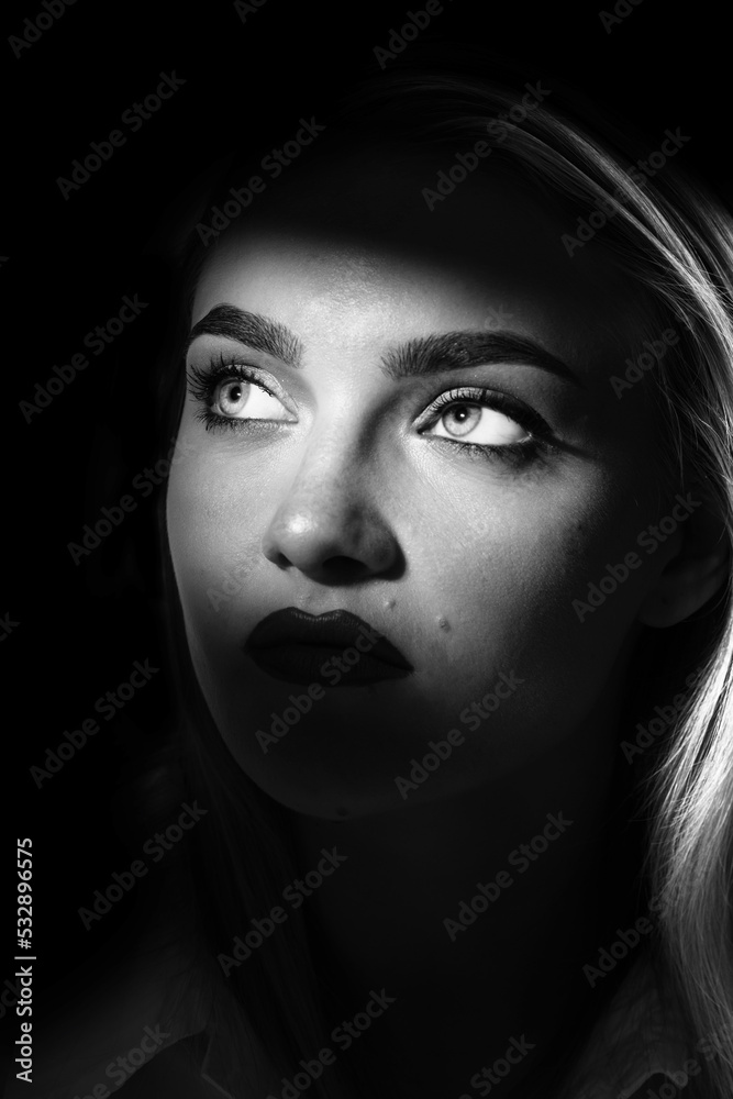 Fashion, style and make-up concept. Beautiful blonde woman portrait partly face covered with shadow. Seductive eyes illuminated with light. Looking up. Black and white image