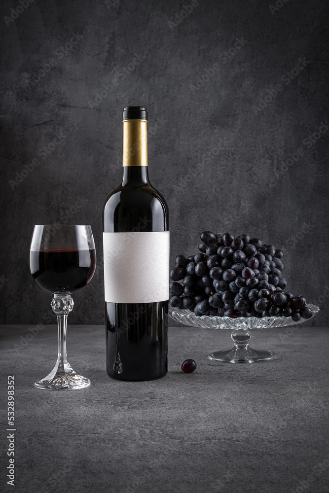 Glass and bottle of red wine with grapes on dark background. Red wine with cheese and fruits. Wine bottle mockup with blank labels to place your design. Space for text