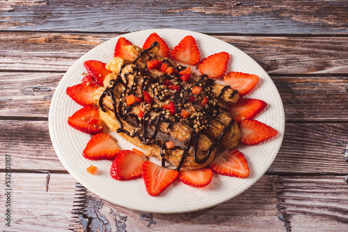Churros with chocolate, crushed almonds and strawberries on a white plate. photo