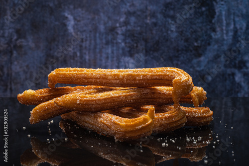 Sugared churros on black table with reflection.