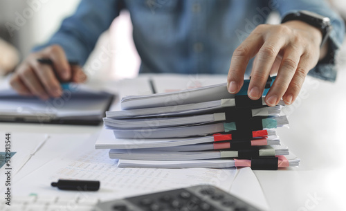 Businessman hands working in Stacks of paper files for searching and checking unfinished document achieves on folders papers