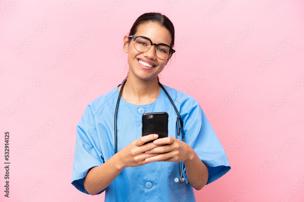 Young nurse Colombian woman isolated on pink background sending a message with the mobile Young nurse Colombian woman isolated on pink background sending a message with the mobile