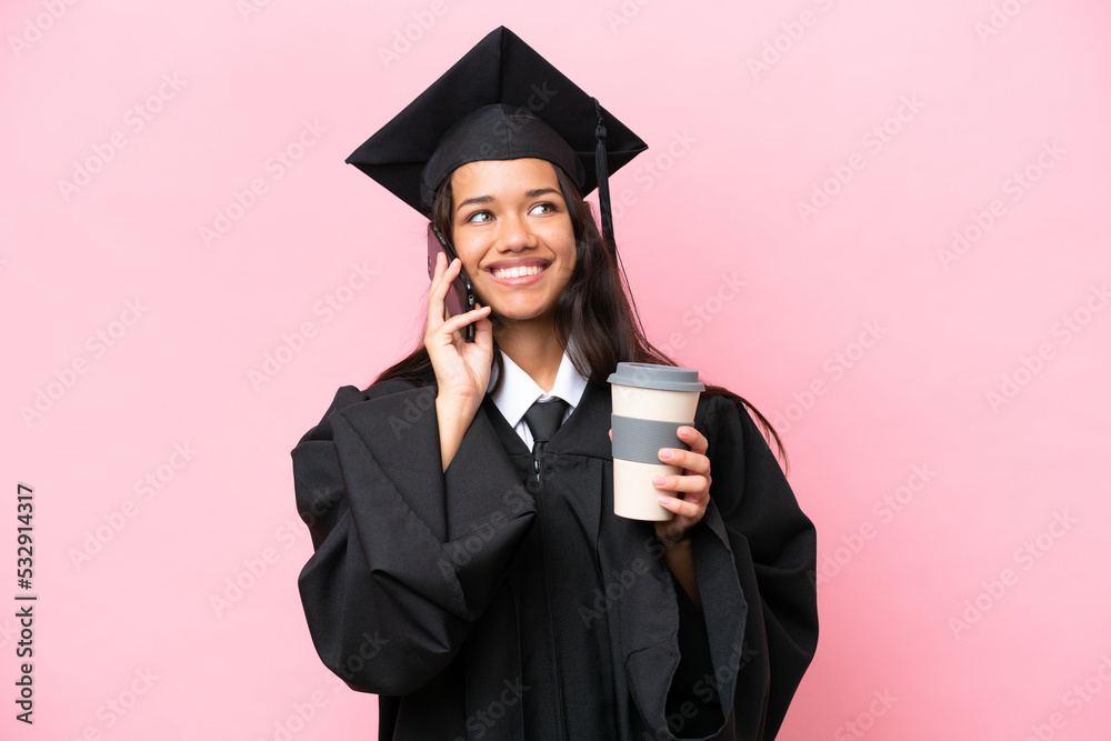 Young university Colombian woman graduate isolated on pink background holding coffee to take away and a mobile Young university Colombian woman graduate isolated on pink background holding coffee to take away and a mobile