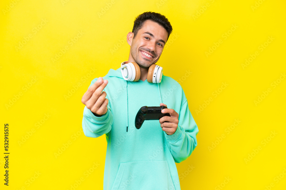 Young handsome man playing with a video game controller over isolated wall making money gesture Young handsome man playing with a video game controller over isolated wall making money gesture