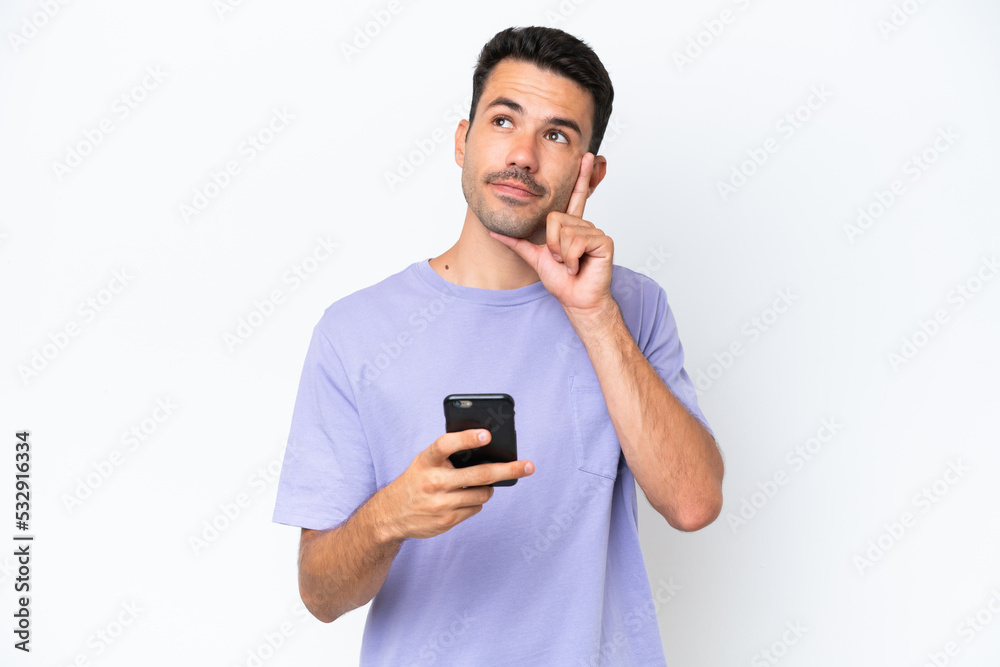 Young handsome man over isolated white background using mobile phone and thinking Young handsome man over isolated white background using mobile phone and thinking