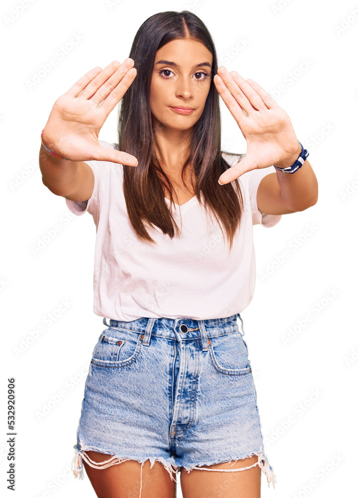 Young hispanic woman wearing casual white tshirt doing frame using hands palms and fingers, camera perspective Young hispanic woman wearing casual white tshirt doing frame using hands palms and fingers, camera perspective