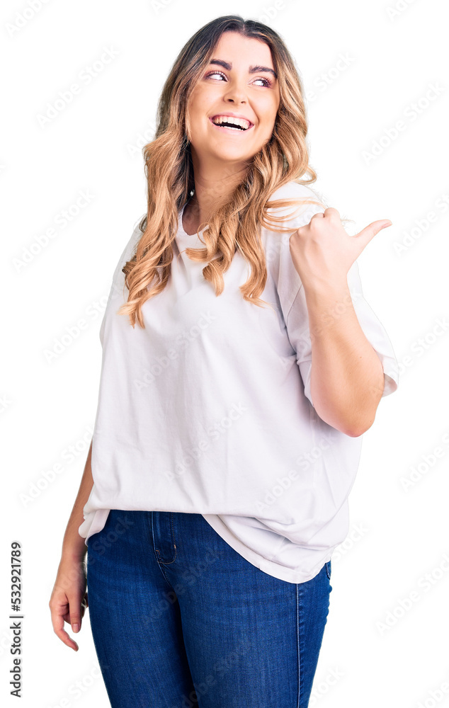 Young caucasian woman wearing casual clothes smiling with happy face looking and pointing to the side with thumb up. Young caucasian woman wearing casual clothes smiling with happy face looking and pointing to the side with thumb up.