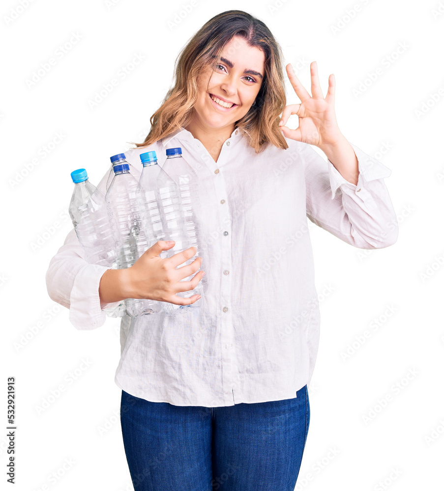 Young caucasian woman holding recycling plastic bottles doing ok sign with fingers, smiling friendly gesturing excellent symbol Young caucasian woman holding recycling plastic bottles doing ok sign with fingers, smiling friendly gesturing excellent symbol