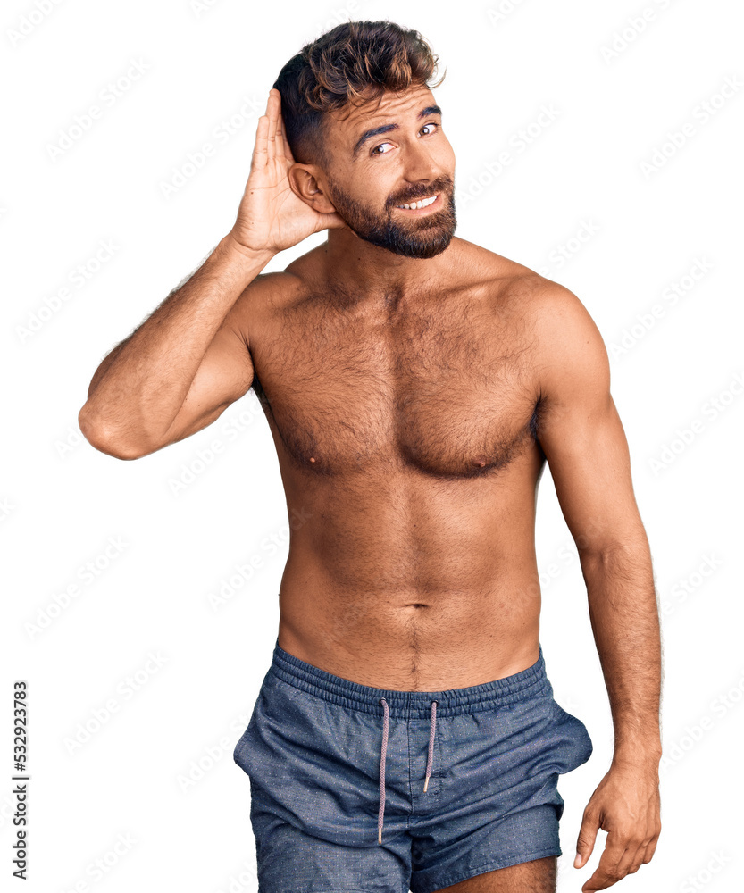 Fototapeta premium Young hispanic man wearing swimwear shirtless smiling with hand over ear listening an hearing to rumor or gossip. deafness concept.