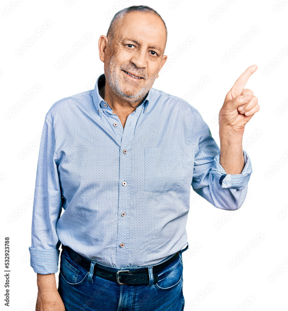 Senior man with grey hair and beard wearing casual blue shirt with a big smile on face, pointing with hand and finger to the side looking at the camera. Senior man with grey hair and beard wearing casual blue shirt with a big smile on face, pointing with hand and finger to the side looking at the camera.